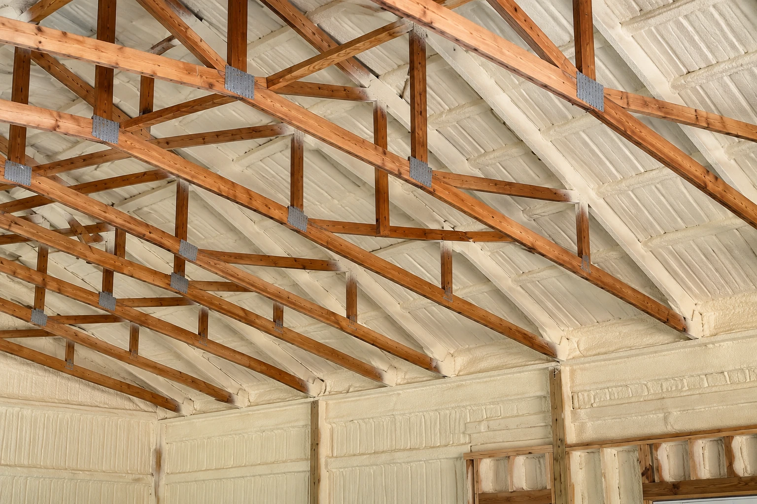 Closed-cell foam coats the roof and walls beneath exposed wooden roof trusses.