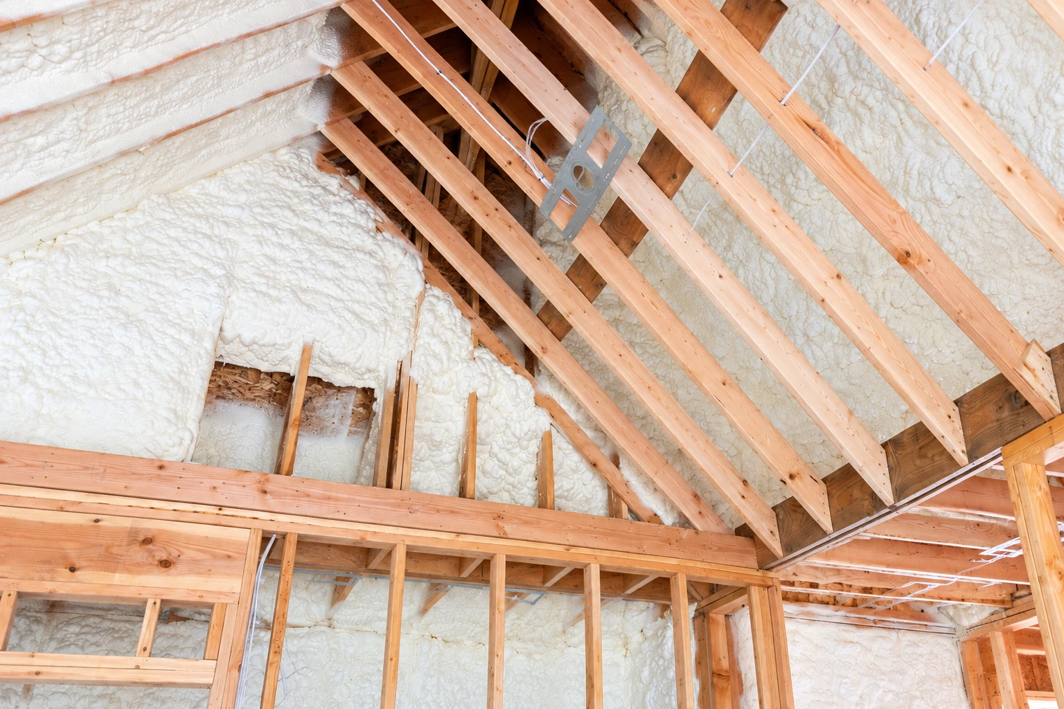 Open-cell spray foam fills the walls and roof of a timber-framed attic, with exposed rafters crossing the view.